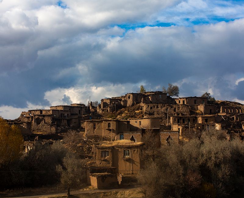 Mud-brick village houses on a hillside under a cloudy sky
