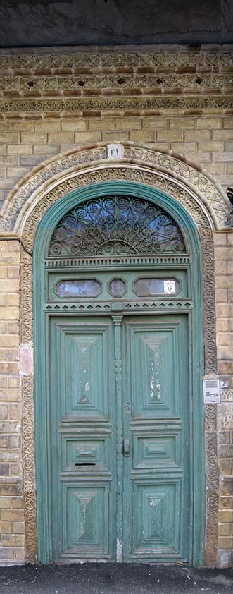Old wooden door painted teal, set in a brick archway